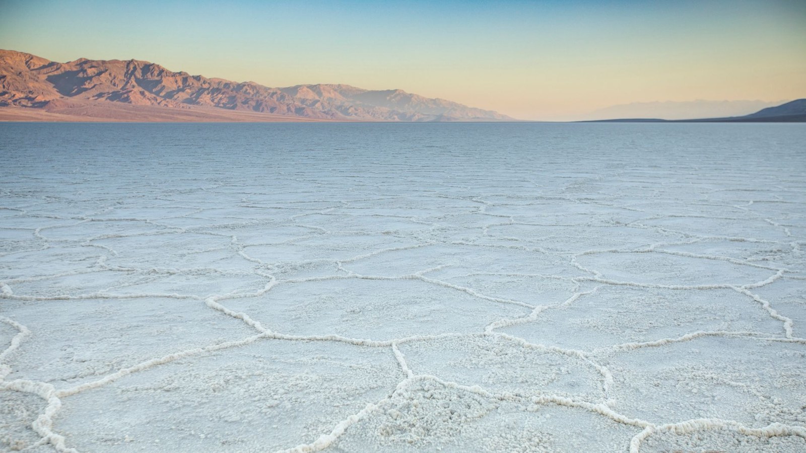 Cracked white salt polygons on the Badwater Basin salt flat in Death Valley with mountains behind