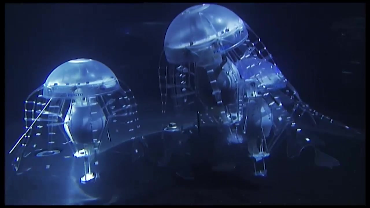Two blue-lit AquaJelly research robots moving through water with tentacle-like structures