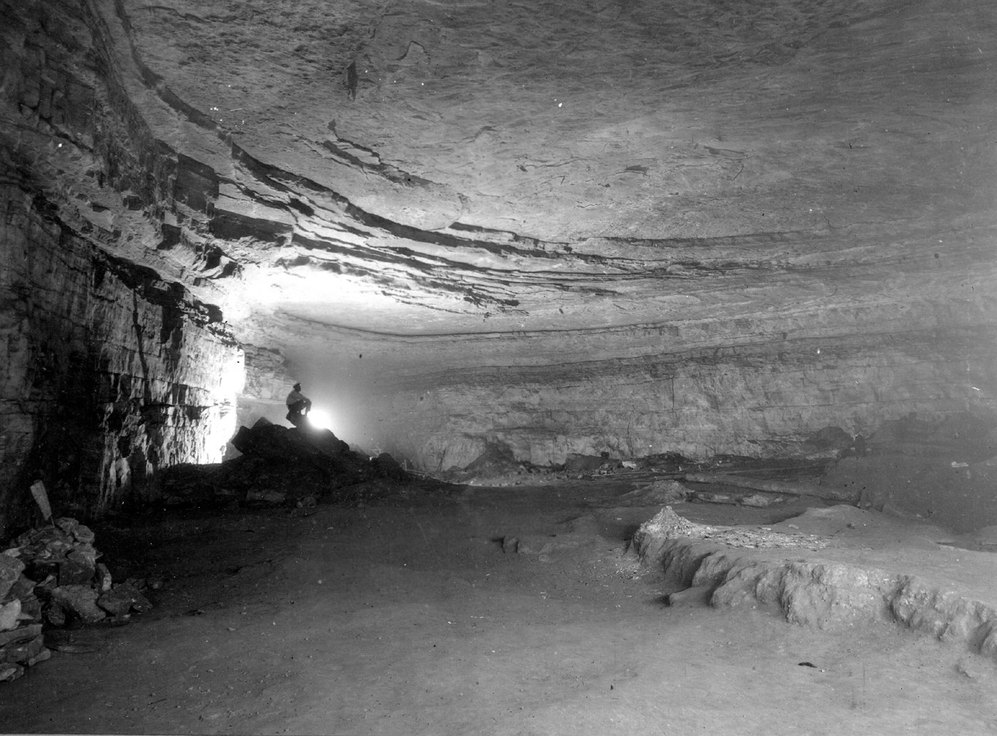 A large passage inside Mammoth Cave with a distant person standing in the lamp light