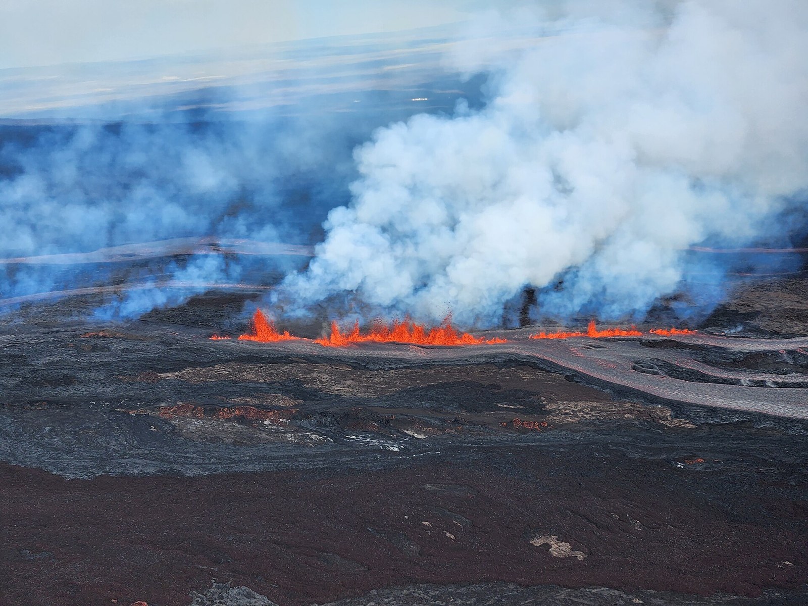 Lava erupting from a fissure on the northeast rift zone of Mauna Loa with a plume of steam