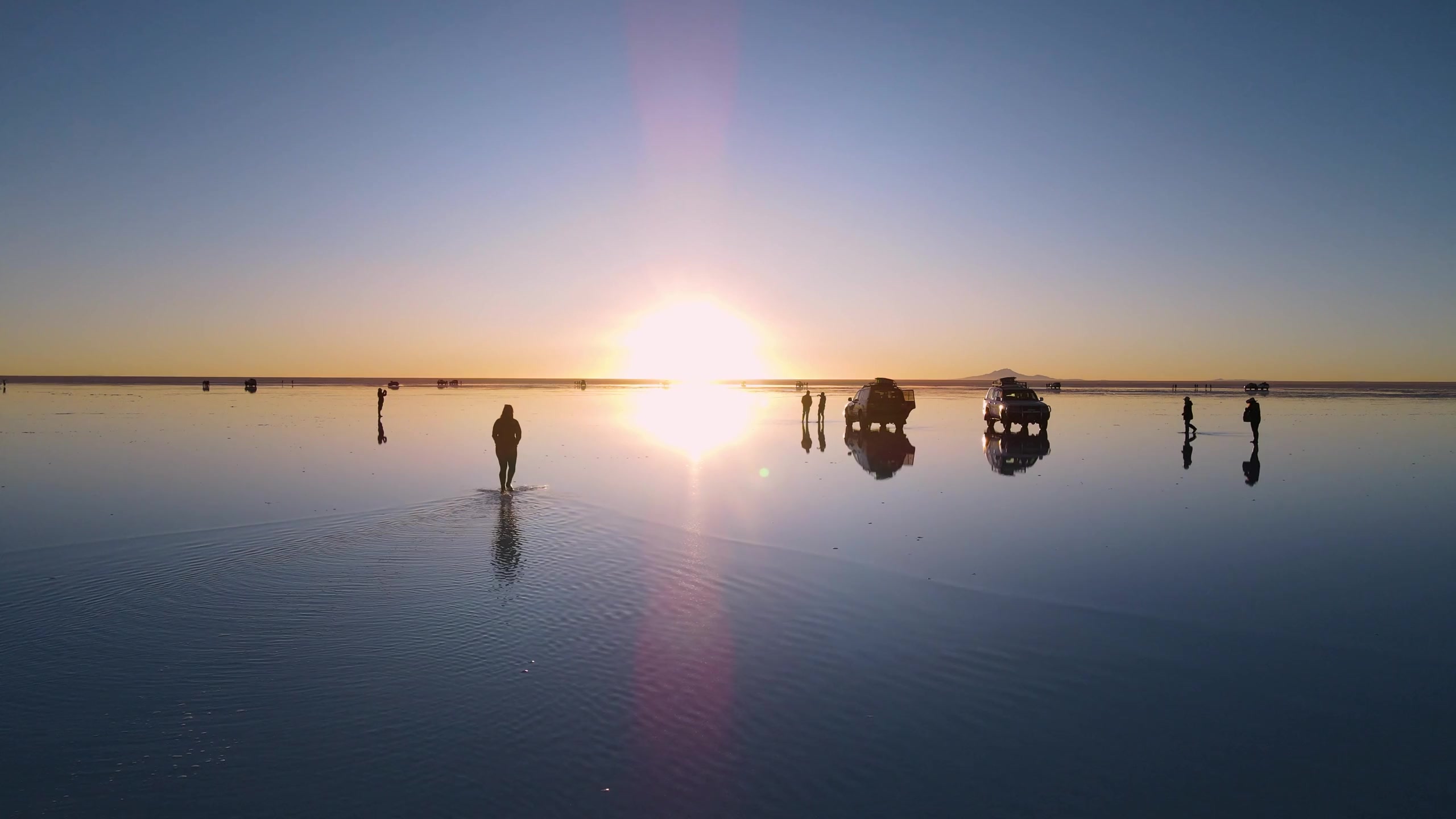 People and vehicles reflected in shallow water on Salar de Uyuni in southwestern Bolivia